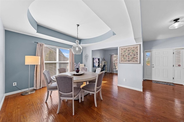 dining area with a raised ceiling, baseboards, and wood finished floors