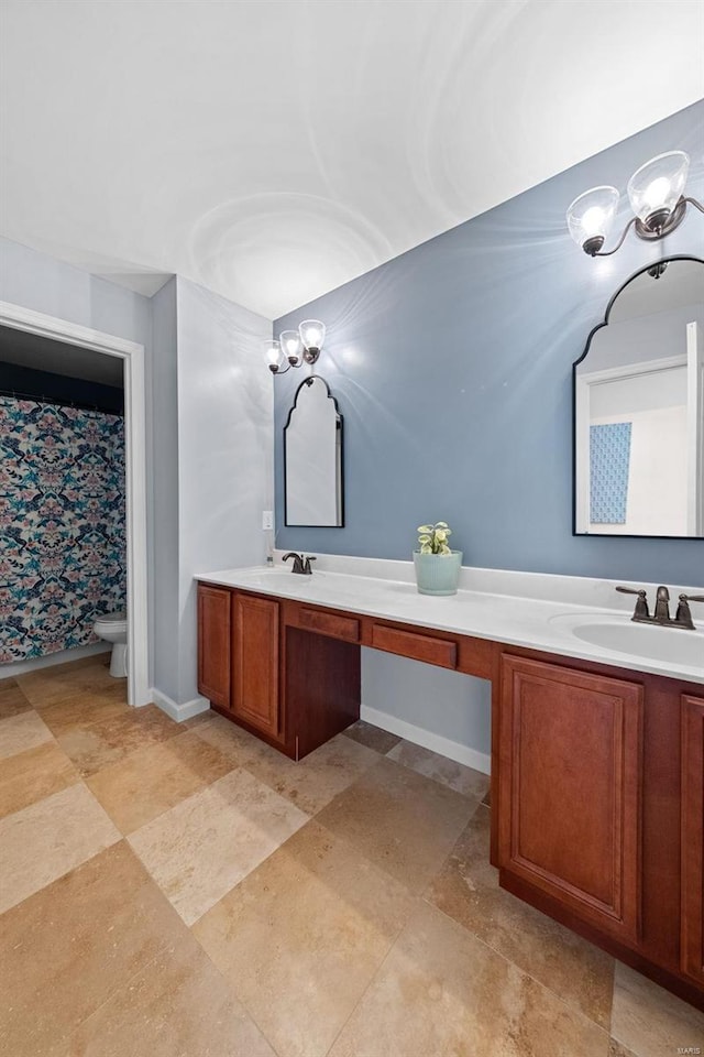 full bath featuring double vanity, a sink, toilet, and baseboards