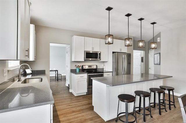 kitchen with a sink, white cabinetry, appliances with stainless steel finishes, a center island, and dark countertops