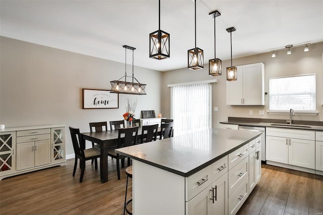 kitchen with dark countertops, hanging light fixtures, white cabinetry, a kitchen island, and a sink