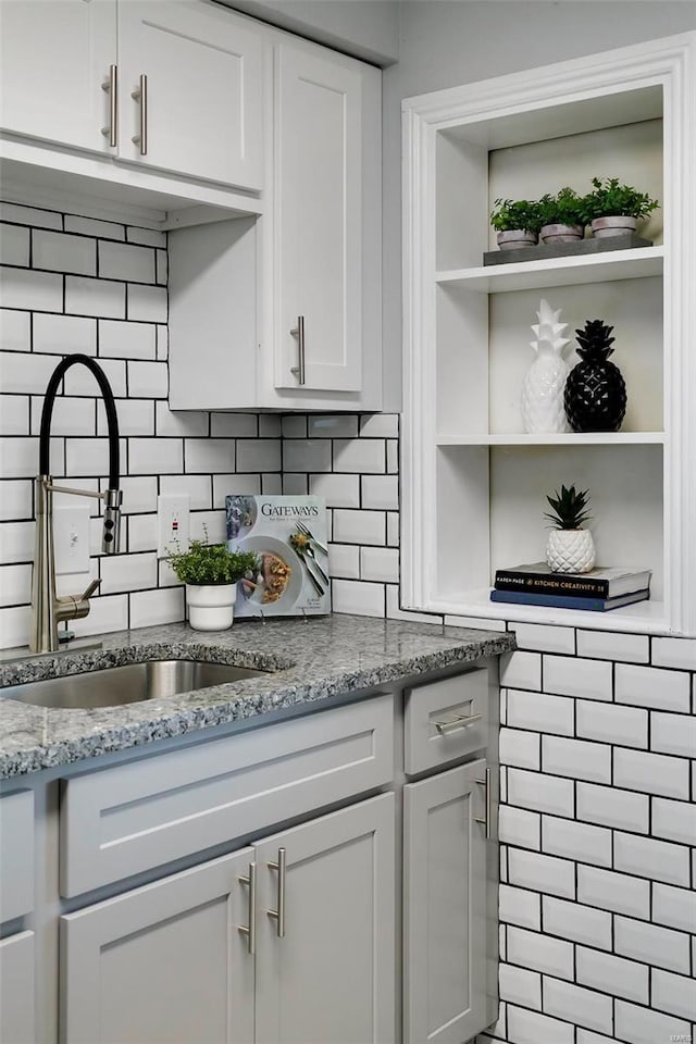 kitchen featuring tasteful backsplash, white cabinetry, sink, and light stone counters