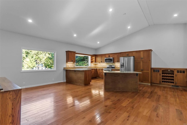 kitchen with backsplash, light hardwood / wood-style flooring, a center island, and appliances with stainless steel finishes