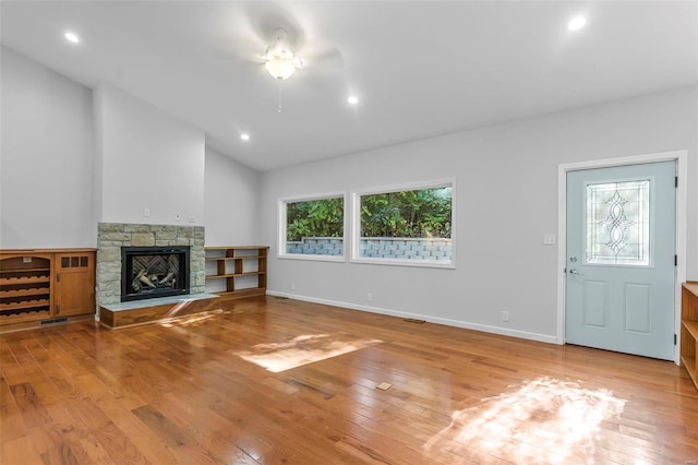 unfurnished living room with lofted ceiling, a stone fireplace, and light wood-type flooring