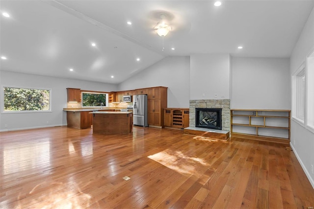 unfurnished living room with a stone fireplace, high vaulted ceiling, and light hardwood / wood-style floors