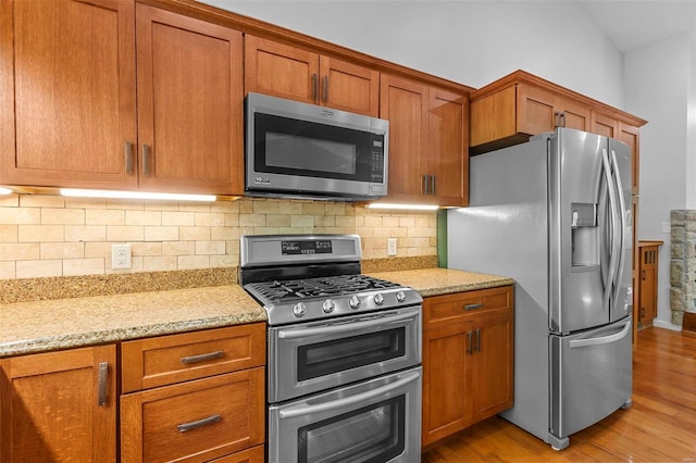 kitchen with stainless steel appliances, light stone countertops, decorative backsplash, and light wood-type flooring