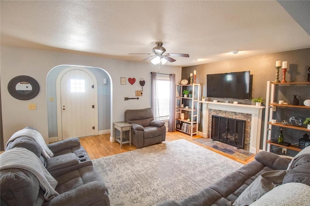 living room featuring a tile fireplace, ceiling fan, a textured ceiling, and light hardwood / wood-style flooring