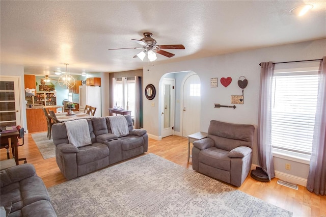 living room with ceiling fan with notable chandelier, light hardwood / wood-style flooring, and a textured ceiling