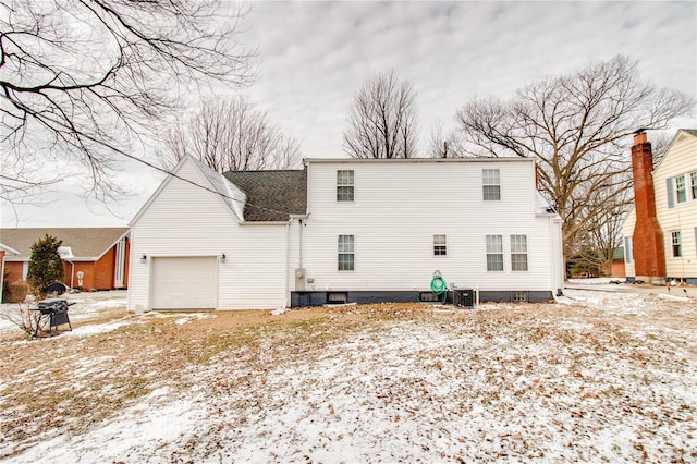 snow covered rear of property featuring a garage and central air condition unit