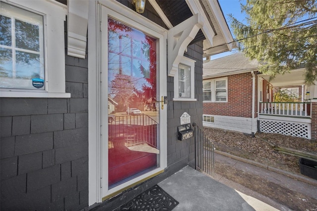 doorway to property featuring covered porch, brick siding, and a shingled roof