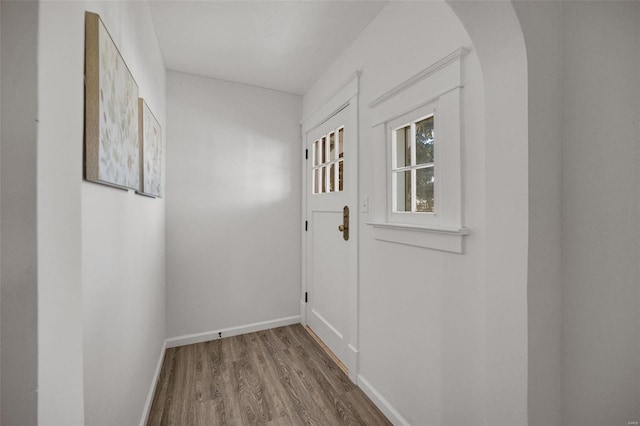 doorway to outside with baseboards, arched walkways, and wood finished floors