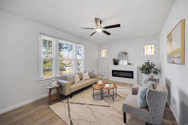 living room with ceiling fan, a glass covered fireplace, wood finished floors, and baseboards