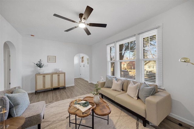 living room with light wood-type flooring, baseboards, arched walkways, and ceiling fan