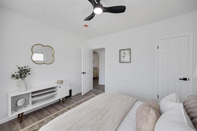 bedroom with arched walkways, ceiling fan, a textured ceiling, wood finished floors, and baseboards