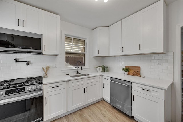 kitchen with stainless steel appliances, a sink, white cabinets, decorative backsplash, and light wood finished floors