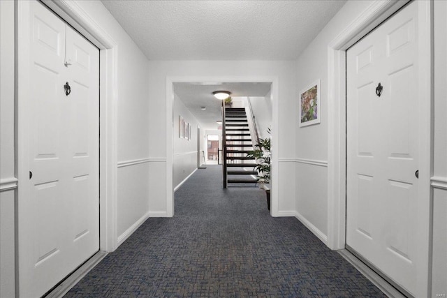 hall featuring a textured ceiling and dark carpet