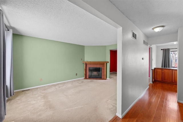 hall featuring visible vents, a textured ceiling, baseboards, and wood finished floors