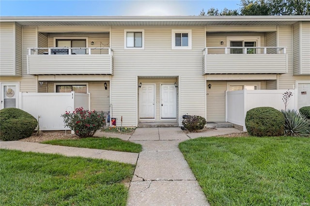 multi unit property featuring a front lawn, fence, and a balcony