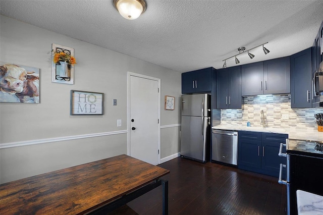 kitchen featuring dark wood finished floors, blue cabinetry, backsplash, appliances with stainless steel finishes, and a sink