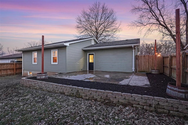 back of house at dusk featuring a fenced backyard and a patio