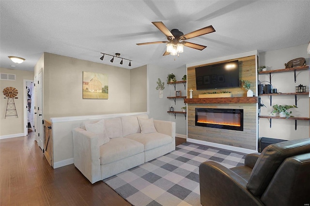 living room featuring visible vents, wood finished floors, a textured ceiling, and a glass covered fireplace