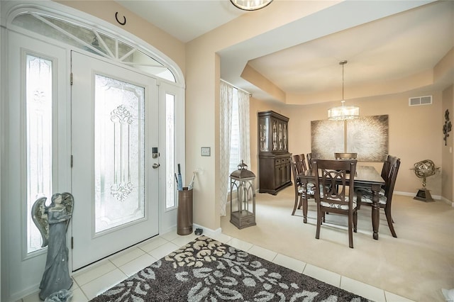 foyer entrance featuring light tile patterned floors, baseboards, visible vents, a raised ceiling, and a notable chandelier