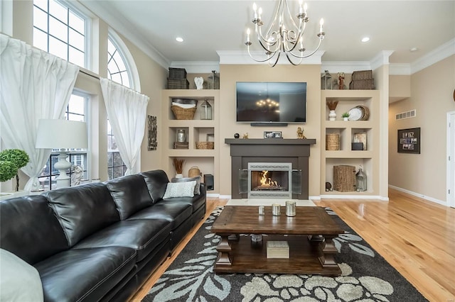 living area with a fireplace with flush hearth, built in shelves, visible vents, and crown molding