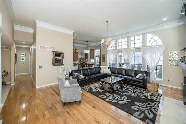 living area featuring a notable chandelier, visible vents, light wood-style flooring, ornamental molding, and a fireplace with flush hearth