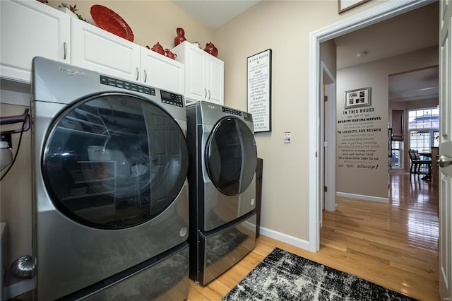 clothes washing area with washer and dryer, cabinet space, light wood-style flooring, and baseboards