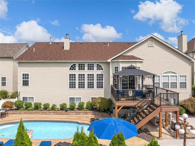 rear view of property with a gazebo, stairway, a wooden deck, a fenced in pool, and a chimney