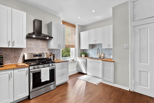 kitchen featuring wall chimney range hood, wood counters, stainless steel appliances, and dark wood-style flooring