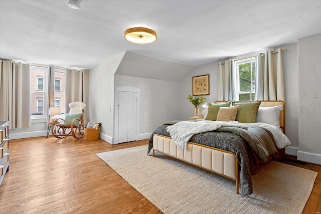 bedroom featuring a textured ceiling, baseboards, vaulted ceiling, and light wood finished floors