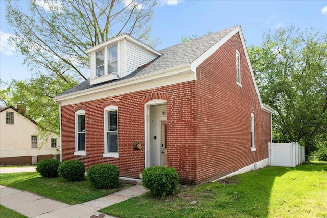 view of front of property with brick siding, fence, a shingled roof, and a front lawn