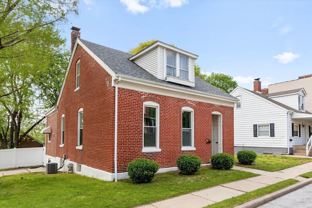 view of front facade featuring central air condition unit, fence, a front yard, and brick siding