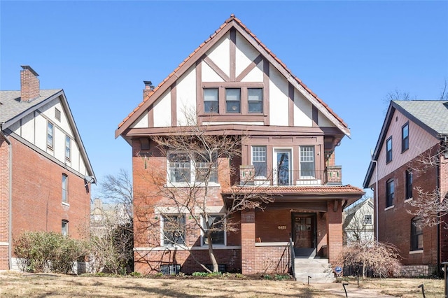 english style home with a balcony, a porch, and brick siding