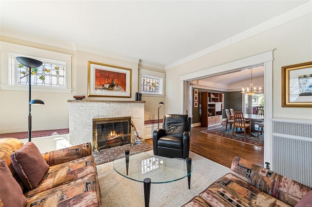 living area with a notable chandelier, wood finished floors, baseboards, ornamental molding, and a brick fireplace