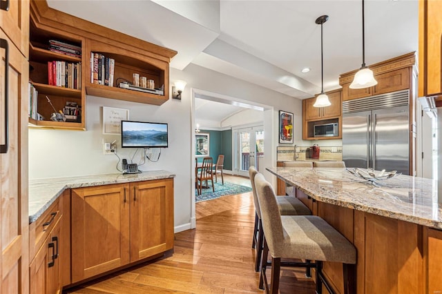 kitchen with brown cabinetry, light wood-style flooring, a kitchen breakfast bar, decorative light fixtures, and built in appliances