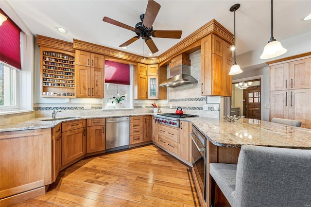 kitchen with wall chimney exhaust hood, light wood-style flooring, a peninsula, stainless steel appliances, and a sink