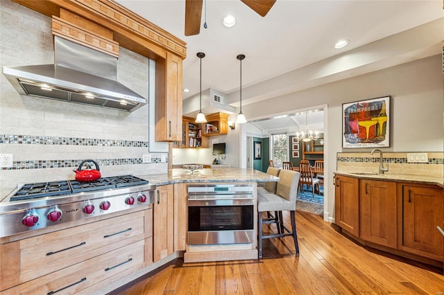 kitchen with visible vents, wall chimney exhaust hood, appliances with stainless steel finishes, light stone counters, and a sink