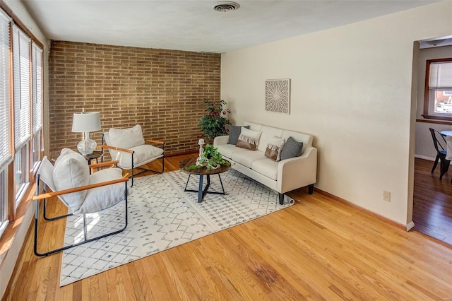 living room with brick wall, plenty of natural light, and wood finished floors