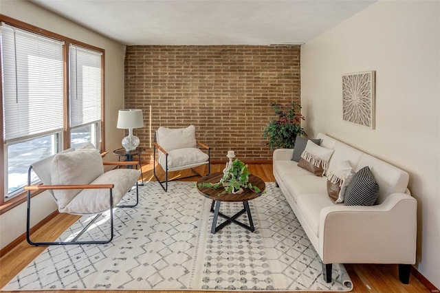 living area featuring light wood-style floors, baseboards, and brick wall