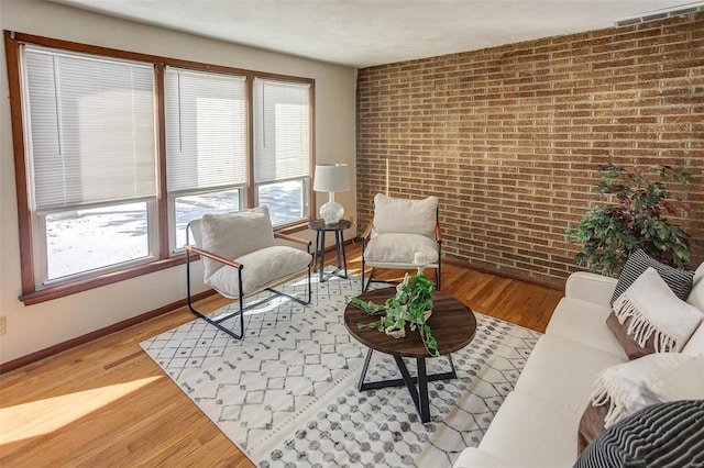 sitting room with baseboards, visible vents, brick wall, and wood finished floors