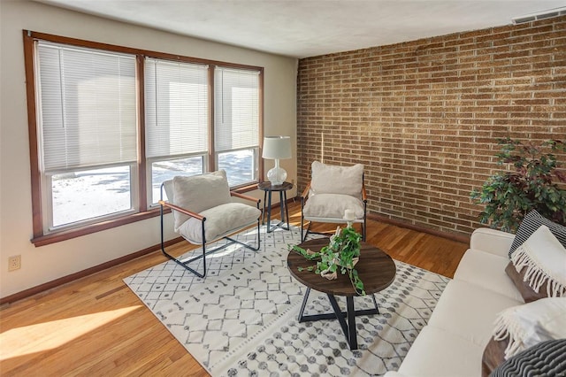 living area featuring baseboards, visible vents, brick wall, and wood finished floors