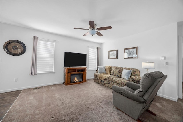 carpeted living area with a glass covered fireplace, baseboards, visible vents, and ceiling fan