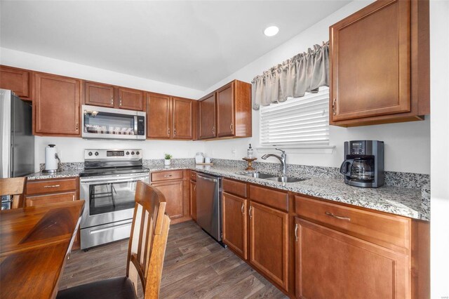 kitchen featuring light stone counters, dark wood-style flooring, appliances with stainless steel finishes, brown cabinetry, and a sink