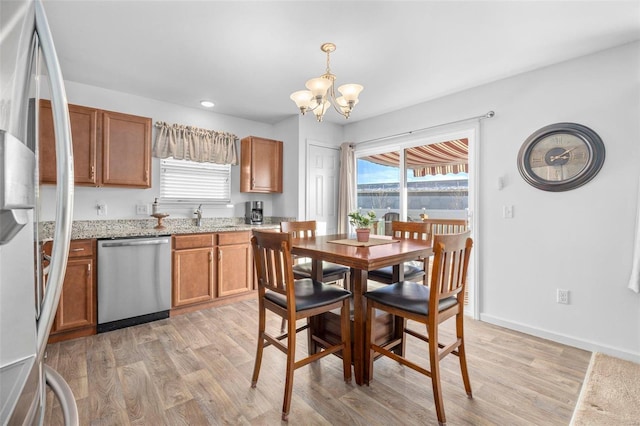 kitchen with a chandelier, stainless steel appliances, a healthy amount of sunlight, brown cabinets, and light wood finished floors