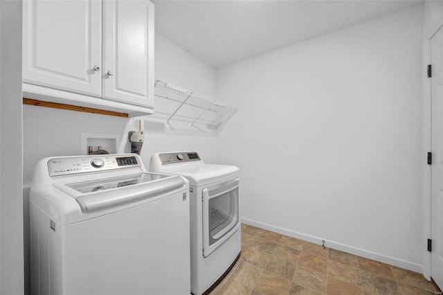 laundry area with stone finish floor, washing machine and clothes dryer, cabinet space, and baseboards