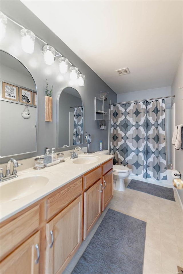 bathroom with toilet, double vanity, a sink, and visible vents