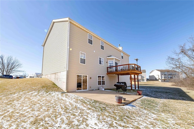 snow covered back of property with a yard, a wooden deck, and a patio