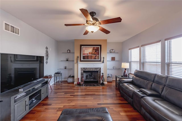 living room featuring dark wood finished floors, visible vents, a ceiling fan, a high end fireplace, and baseboards