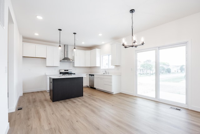 kitchen featuring wall chimney exhaust hood, a kitchen island, white cabinetry, and light countertops